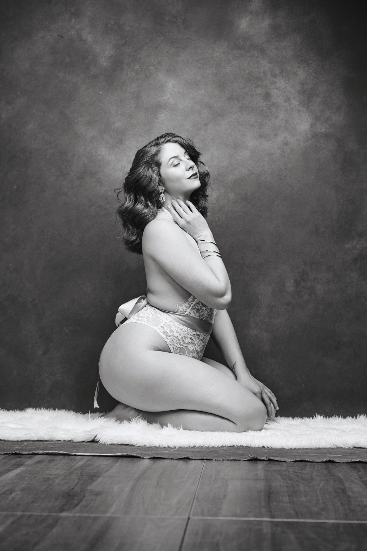 Black-and-white boudoir portrait kneeling in lace bodysuit on studio floor