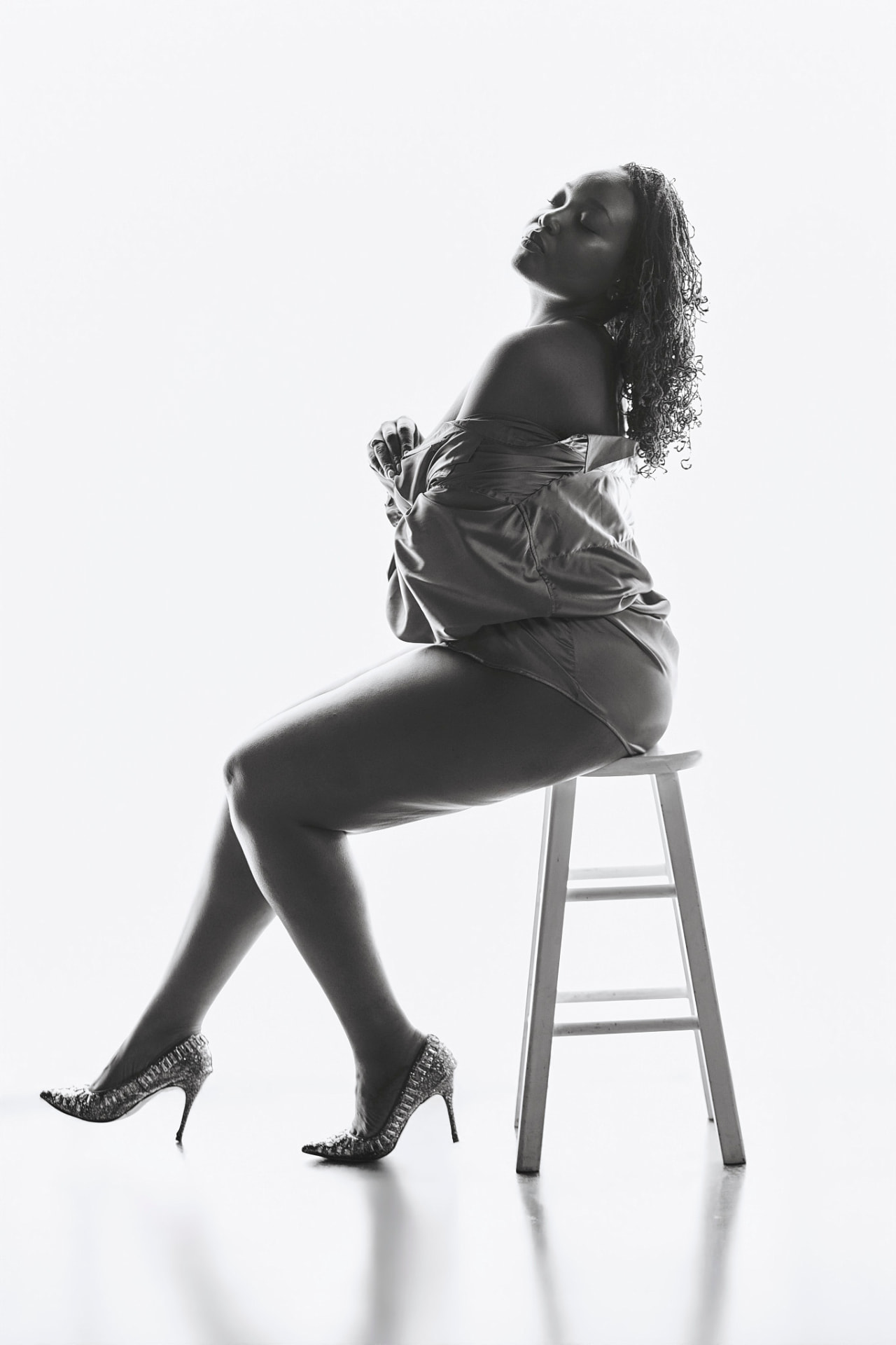 Black-and-white boudoir portrait seated on a stool against a bright backdrop